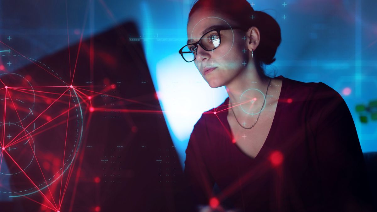 Egy nő programozás közben, számítógép előtt, technológiai háttérrel.