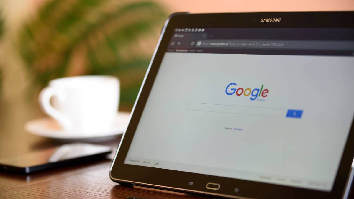 Egy tablet képernyőjén a Google keresőoldala látható, háttérben egy kávéscsésze.