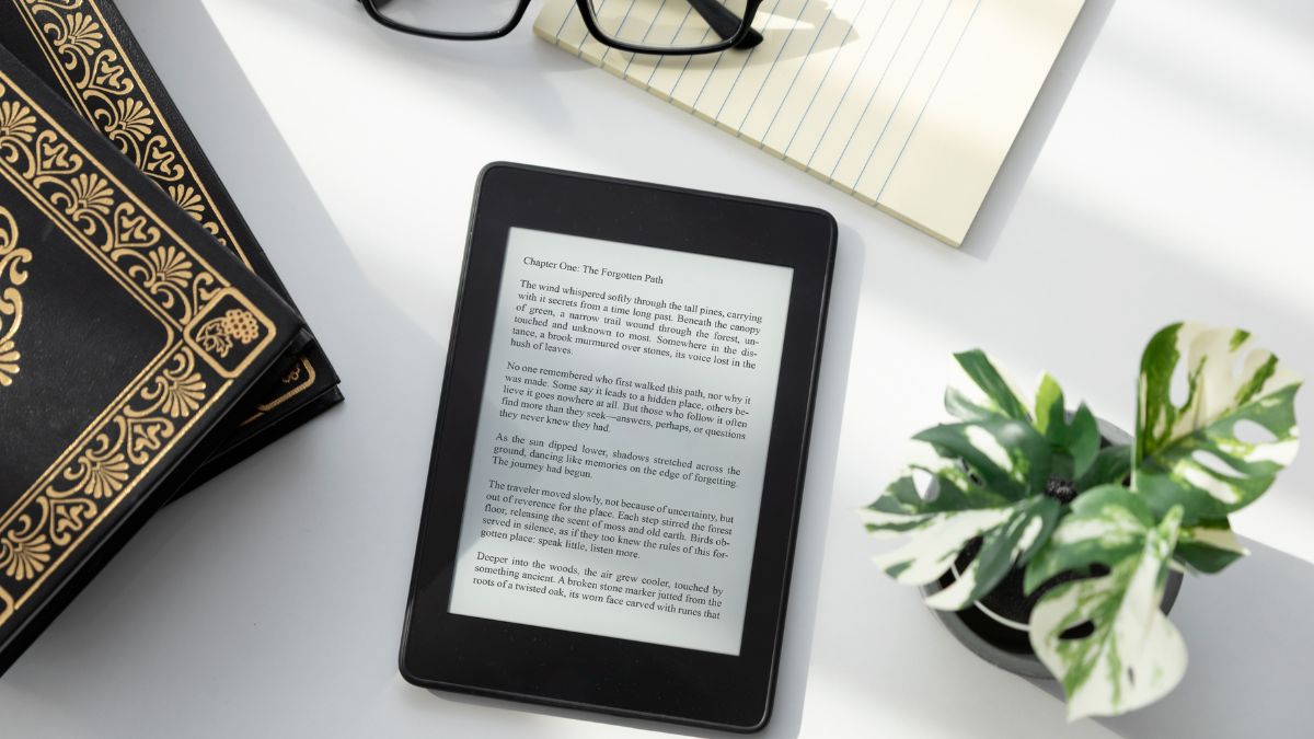 Egy e-book olvasó, mellette könyvek és egy jegyzetfüzet, világos asztalon.