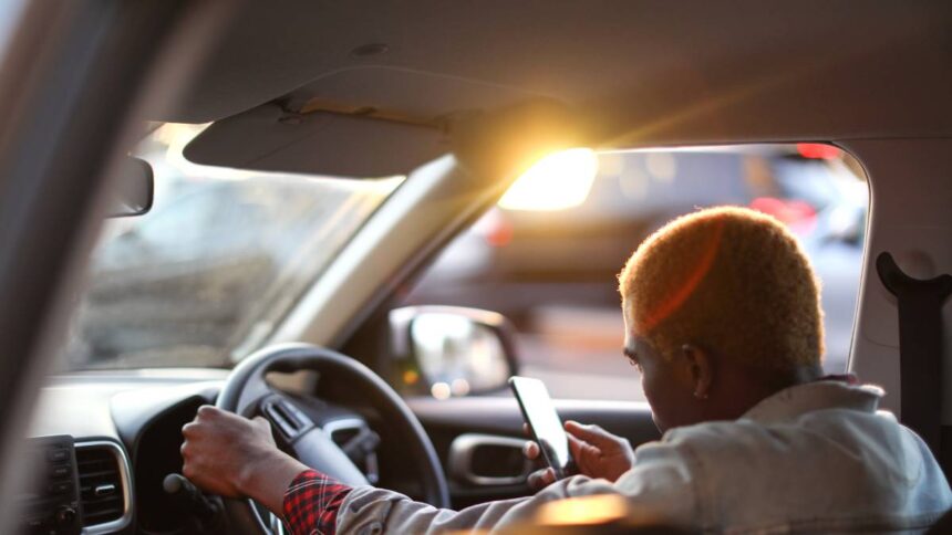 Egy utas ül az autóban, telefonján az Uber alkalmazást használja.